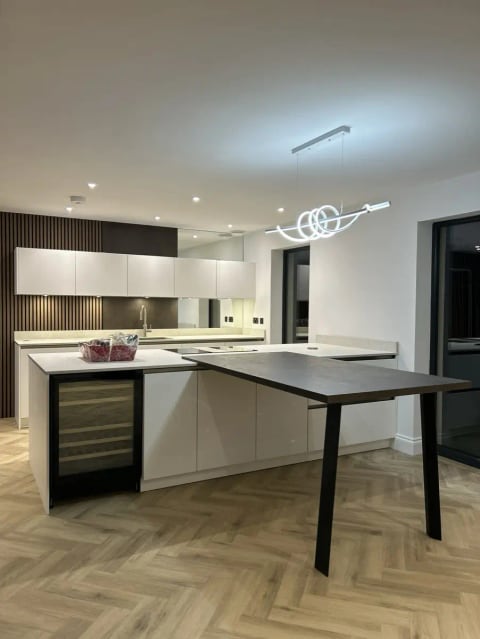 Finished kitchen with white units, a dark breakfast bar and herringbone floor